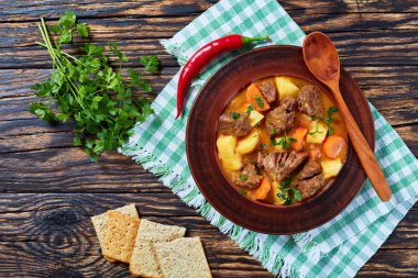 beef stew with vegetables in a spicy gravy or estofado de carne in a clay bowl on a wooden table,spain cuisine, view from above, close-up, flatlay clipart