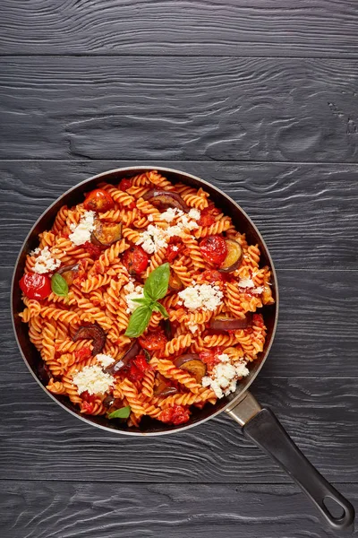 意大利面食 Fusilli 与茄子 西红柿 清酪干酪在一个黑色的木桌上的煎锅 垂直视图从上面 — 图库照片