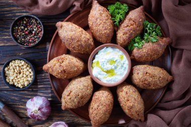 deep fried kibbeh of ground beef meat mixed with bulgur, stuffed with fried minced meat with pine nuts, spices, garlic and herbs on a clay plate on an old dark wooden table, close-up, flat lay clipart