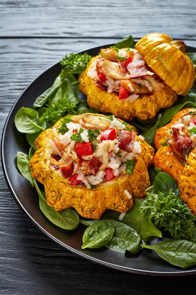 baked Patty Pan squash stuffed with rice, fried chicken meat, crispy fried bacon, bell pepper and served with green fresh spinach leaves and parsley on a black plate, vertical view from above