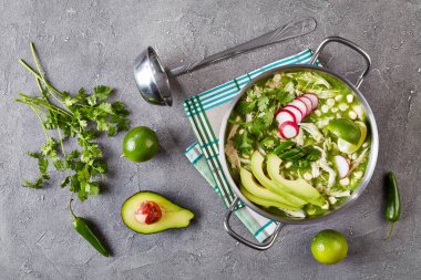 Chicken Pozole Verde - Mexican stew filled with shredded chicken and hominy in a warm green chile broth garnished with radish and avocado slices, fresh green coriander and a lime clipart