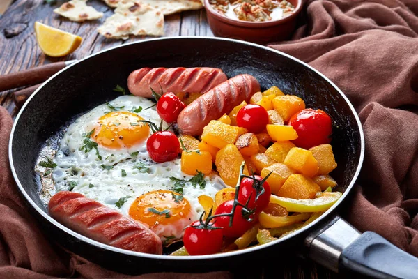 Autumn meal set: sunny side eggs, maple glazed pumpkin, roasted sausages, tomatoes with baba ganoush dip made from baked eggplant with tahini, olive oil, lemon juice on a wooden background, close up