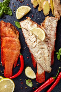 fillet of hot smoked red snapper on a black stone plate with spices, herbs and sliced lemons, vertical view from above, close-up clipart