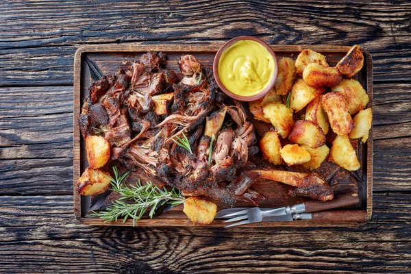 overhead view of delicious slow roast tender leg of lamb pulled off the bones and  served with crispy roast potatoes on a wooden tray on a rustic wooden table,view from above, flatlay