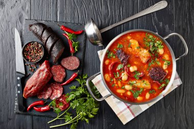 hearty Fabada Asturiana Bean Stew with chorizo, bacon and blood sausages in a metal casserole on a black wooden table with ingredients on a cutting board, spanish cuisine, view from above, flatlay clipart