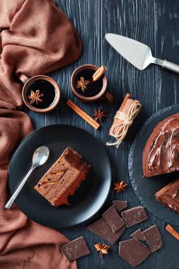 a slice of chocolate Cake with apricot jam filling topped with Chocolate Ganache served on a plate with mulled wine in clay rustic cups on a black wooden table, vertical view from above, flatlay clipart