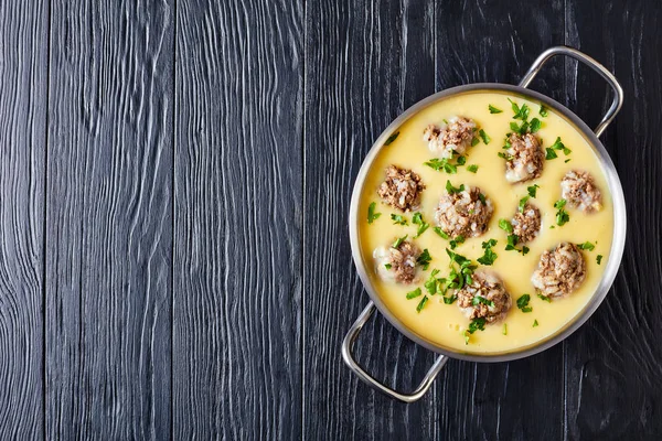 - Giouvarlakia, Youvarlakia in Egg lemon sauce in a metal casserole on a black wooden table, view from above, flatlay, copy space — Stock Image Giouvarlakia Youvarlakia Egg Lemon Sauce Metal Casserole Black Wooden Table Stock Photo