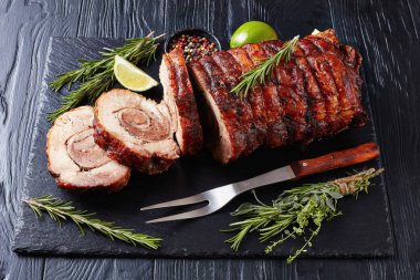 overhead view of sliced roast pork roulade -  Porchetta, delicious pork roast of Italian culinary holiday tradition on a slate tray with rosemary and lime, close-up clipart