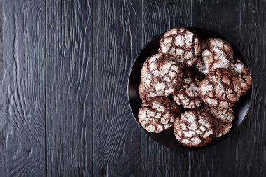 Chocolate Crinkle cookies. Cracked chocolate biscuits. Chocolate biscuits, Christmas cookies on a black plate on a wooden table, view from above, flatlay, copy space clipart