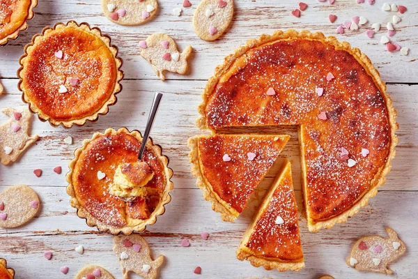 classic Swiss Easter Rice Tart sprinkled with powdered  sugar, gateau de Paques, Osterchuechli in tart shells, on a wooden table with easter cookies, horizontal view from above, flatlay, close-up