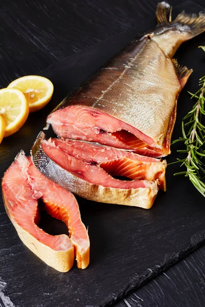 smoked wild salmon cut in steaks with fresh rosemary salt and peppercorn on a black slate plate, view from above, close-up