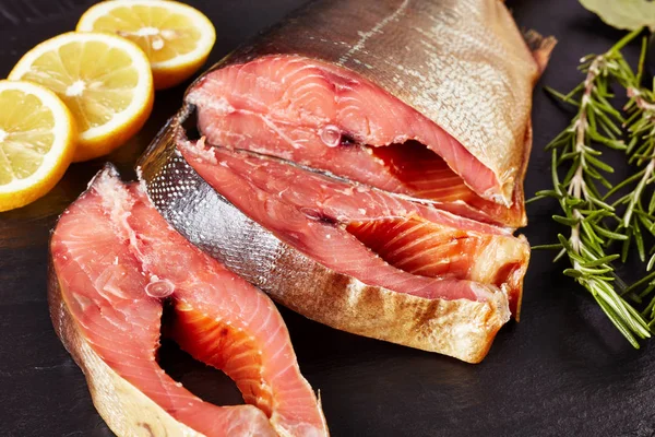 Smoked wild salmon cut in steaks with fresh rosemary salt and peppercorn on a black slate plate, horizontal view from above, close-up, macro — Stock Image Smoked Wild Salmon Cut Steaks Fresh Rosemary Salt Peppercorn Black Stock Picture