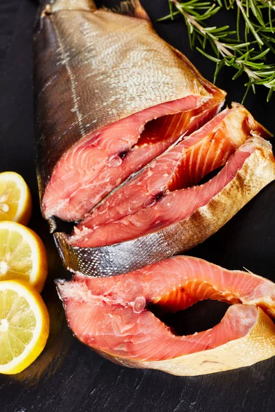 Smoked wild salmon cut in steaks with fresh rosemary salt and peppercorn on a black slate plate, vertical view from above, close-up — Stock Image Smoked Wild Salmon Cut Steaks Fresh Rosemary Salt Peppercorn Black Stock Picture