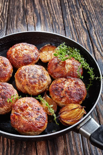 fried turkey, chicken patties, cutlets of minced meat  in a skillet with thyme, garlic and onion on an old wooden table, vertical view from above