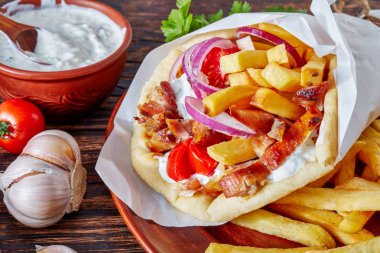 close-up of greek souvlaki, pita ma gyros with chicken meat, vegetables, french fries and yogurt garlic sauce, ingredients on a cutting board on a rustic table, view from above, macro clipart