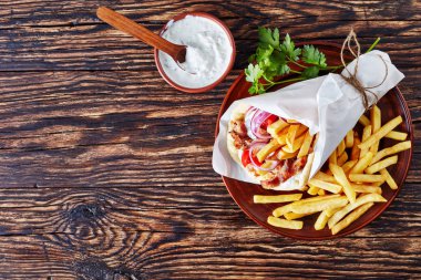 overhead view of greek souvlaki, pita ma gyros with chicken meat, vegetables, french fries on a earthenware plate and tzatziki sauce in a bowl on a rustic table, view from above, flatlay, copy space clipart