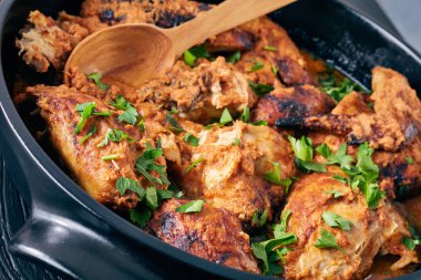overhead view of Kuku Paka, Kenyan chargrilled Chicken in creamy spicy Coconut gravy in a earthenware saucepan on a black wooden table, view from above, close-up clipart