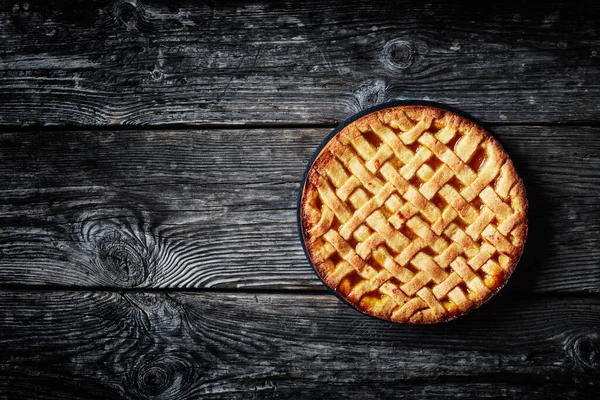 sweet apricot pie with a lattice pie crust topping in a baking shell with on a dark rustic wooden table, flat lay, free space