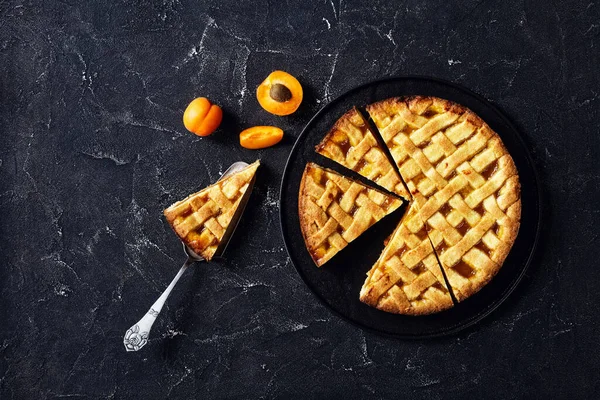 close-up of sliced apricot shortcrust pie with a lattice pie crust topping on a black plate, a slice of pie on a vintage cake shovel on a concrete table, flat lay, free space