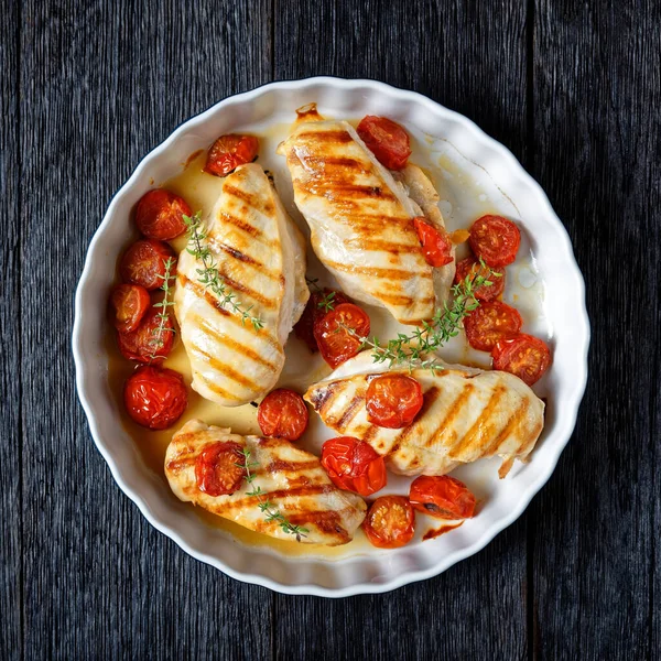 grilled chicken breasts with roasted cherry tomatoes in a baking shell on a dark wooden table, flat lay, free space