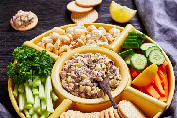 close-up of Tuna capers pickles dip set served with carrots and celery sticks, sliced fresh cucumber, crackers and pork rinds in bowls on a white wooden table, Philippines cuisine