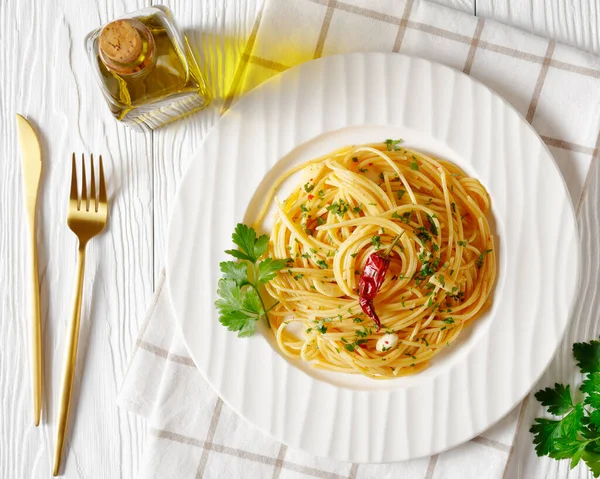Spaghetti Alla colatura di alici, Spaghetti with anchovy sauce, pimento pepper, garlic and parsley on a white plate on a white wooden table, horizontal view from above, flat lay
