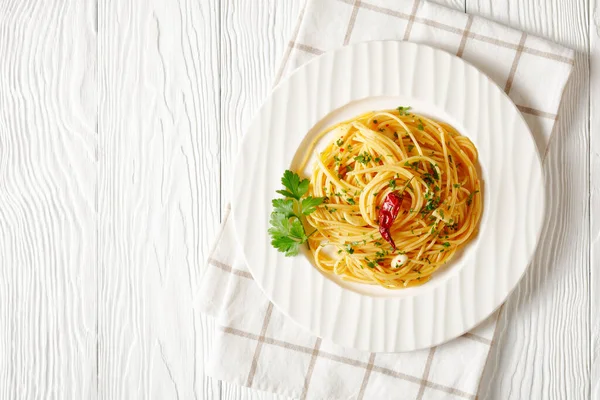 Spaghetti Alla colatura di alici, Spaghetti with anchovy sauce, pimento pepper, garlic and parsley on a white plate on a white wooden table, horizontal view from above, flat lay, free space