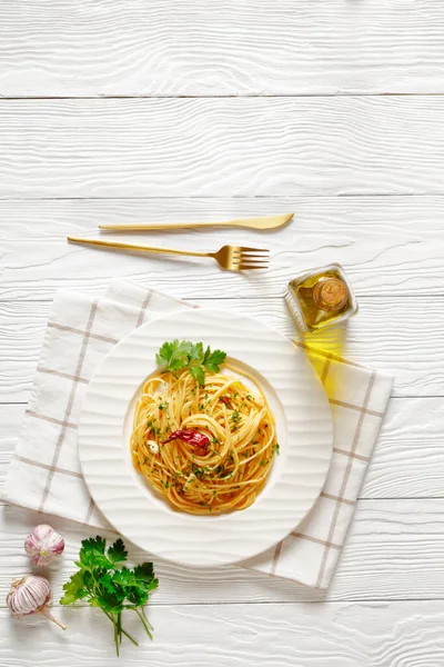 Spaghetti alla colatura, Spaghetti with anchovy sauce, pimento pepper, garlic and parsley on a white plate on a white wooden table, horizontal view from above, flat lay, free space