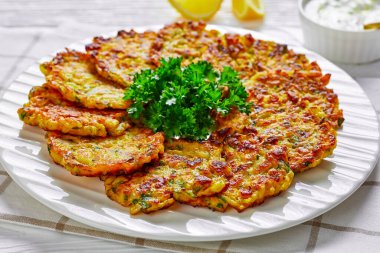 Onion patties latkes with parsley and rice served on a white plate with lemon and greek yogurt sauce on a white wooden background, cutlery, close-up clipart