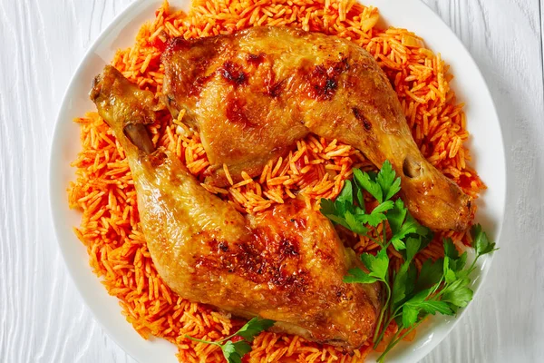 Simple side dish: tomato rice with roasted chicken quarters cooked of basmati rice with red chili powder, cinnamon, cardamom, cloves, parsley on a white plate, top view, close-up