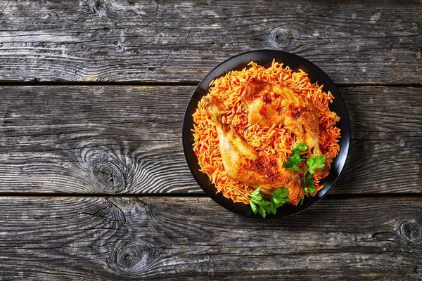 South indian tomato rice cooked with sauteed tomatoes, onion, red chili powder, cinnamon, turmeric with oven-baked chicken quarters on a black plate, on rustic wooden background, top view, copy space
