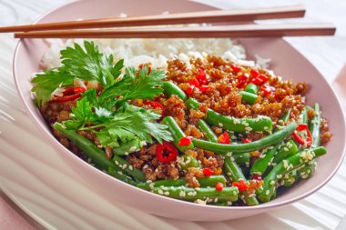Thai pad kra pao: stir-fried pork with long grain rice and green beans sprinkled with sesame seed, red chili served on a pink bowl with chopsticks on a white wooden background, close-up clipart