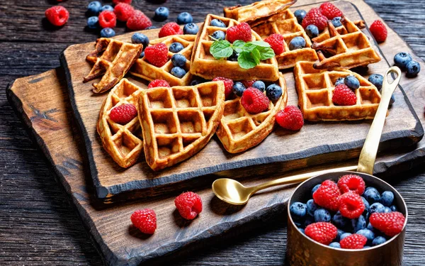 oatmeal banana waffles served with berries and honey on a dark wooden cutting board on a wooden table, horizontal view from above, landscape view from above, close-up