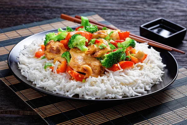 泰国腰果鸡配蔬菜炒 西兰花 热红辣椒和酱油 放在一个黑色盘子里 配上米和筷子 背景是深色的木制 顶部观景 — 图库照片