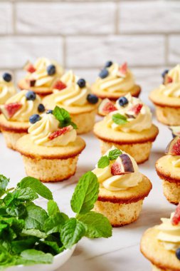 delicious cupcakes with buttercream and fresh berries and mint on a marble table, vertical view from above, close-up clipart