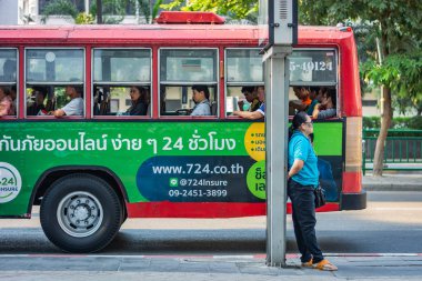 Bangkok, Tayland - Kasım 2018: Kadın sokakta direğe karşı yaslanmış duran, Bangkok, Tayland arka planında kırmızı bir otobüs içinde kişi ile çalışan