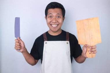 Young smiling asian men wearing apron hold knife and cutting board, preparing to cooking, look camera isolated on white background studio. Cooking food concept.