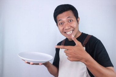 Excited face expression asian man chef or waiter shows empty white plate, presenting something. Isolated white background
