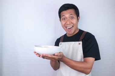 Excited face expression asian man chef or waiter shows empty white bowl, presenting something. Isolated white background