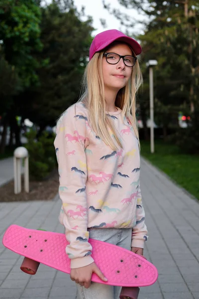 pembe kap ve kaykay parkı ile sarışın kız portresi. Genç kız gözlük Caddesi üzerinde açık havada. Çocukluk, yaz, tatil, spor 
