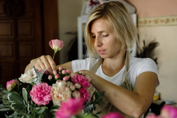 woman florist making bouquet of pink flowers indoor. Female florist preparing bouquet of roses in flower shop. entrepreneurship, small business, workplace concept
