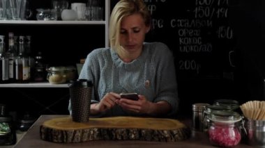 kadın kahve kapalı ve kullanma cep telefonu içme. Kadın cep telefonu kafede üzerinden kısa mesaj gönderme. Ahşap masa üzerinde akıllı telefon kullanan kadın. Yumuşak odak. Ağır çekim