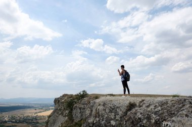 bir uçurumun kenarında duran ve cep telefonuyla genç kadın uzun yürüyüşe çıkan kimse. Kadın turist alarak fotoğraf dağın zirvesinde. Seyahat, özgürlük, tatil, trekking, hiking kavramı
