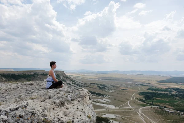 年轻女子坐在悬崖的顶峰 期待平原 女性徒步旅行者在山顶和欣赏风景 禅宗概念 — 图库照片