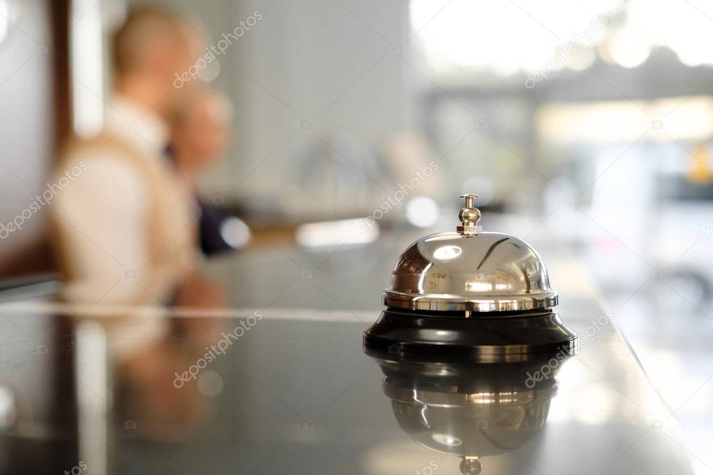 Modern luxury Hotel Reception Counter desk with Bell. Service Bell locating at reception. Silver Call Bell on table, Receptionists on background. heck in hotel. Concept. 