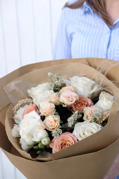 Bouquet of white and beige Roses. Woman Florist holding bouquet of Flowers indoor. Female florist preparing bouquet in flower shop. Close up. Mother\'s Day and Valentine\'s Day concept