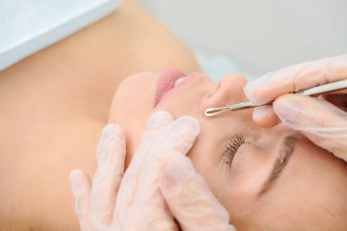 Siyahların ve sivilcelerin derilerini çelik aletlerle temizleme prosedürü. Güzellik salonunda siyah başlık çıkarıcı ile kadın yüzünün derin temizlenmesi. Kozmetik uzmanı temizlik terapisi alıyor. 