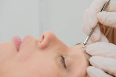 Siyahların ve sivilcelerin derilerini çelik aletlerle temizleme prosedürü. Güzellik salonunda siyah başlık çıkarıcı ile kadın yüzünün derin temizlenmesi. Kozmetik uzmanı temizlik terapisi alıyor. 