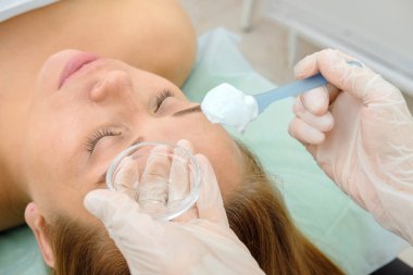 Yüz peeling maskesi, spa güzellik bakımı, Cilt Bakımı. Yüz bakım spa Salonu Güzellik Uzmanı tarafından Başlarken kadın. Güzellik uzmanı bir kız hasta yüzünde krem maske uygulanıyor. Kozmetik. Yakın çekim