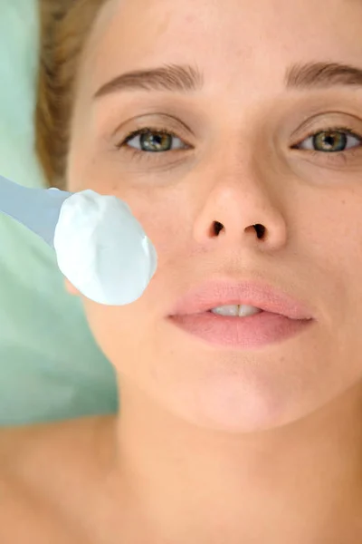 Face peeling mask, spa beauty treatment, skincare. Woman getting facial care by beautician at spa salon. Cosmetologist applying  cream mask on face of a girl patient. Cosmetology.  Close up